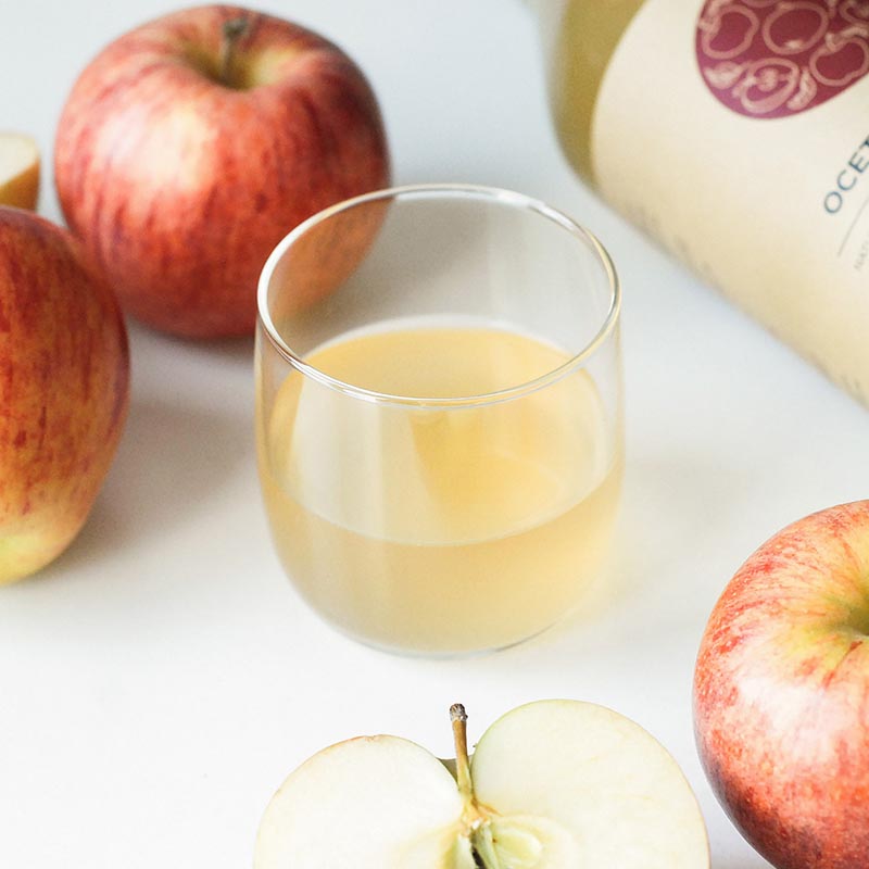 szklanka mętnego octu jabłkowego marki Racjonalni, w otoczeniu jabłek