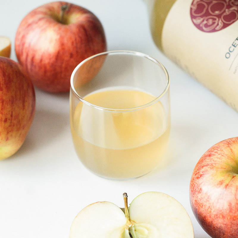 przepis na naturalny ocet jabłkowy - szklanka mętnego, żywego, niepasteryzowanego octu jabłkowego Racjonalni, w tle jabłka i butelka octu jabłkowego